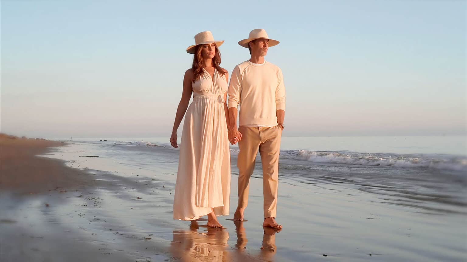 A couple walking down a beach at sunset.